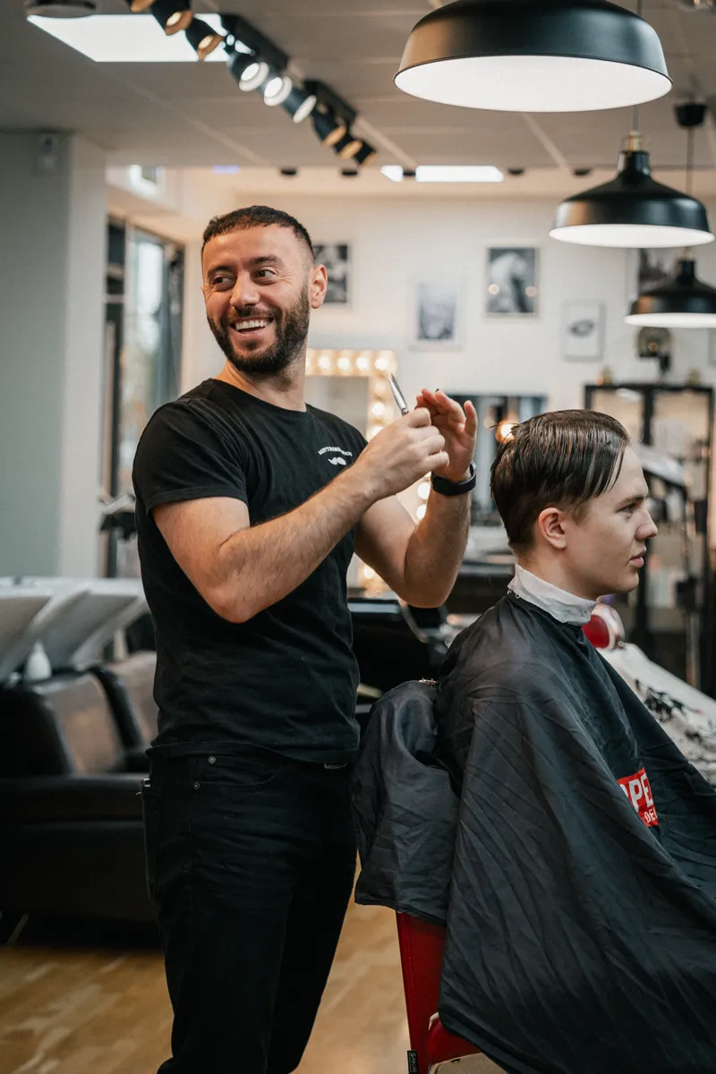 Barberare klipper kund med sax - Samy's Barbershop Solna